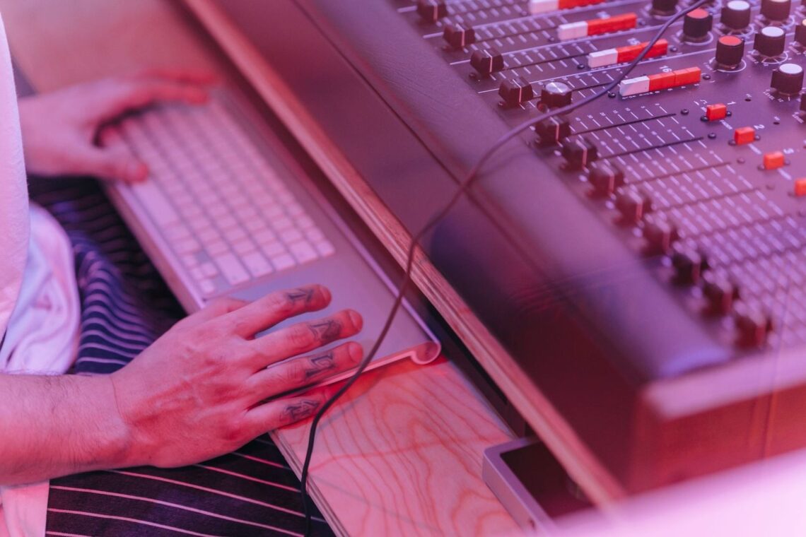 Musiker arbejder ved et keyboard og en analog mixerpult i pink lys