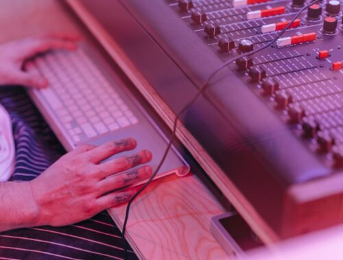 Musiker arbejder ved et keyboard og en analog mixerpult i pink lys