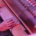 Musiker arbejder ved et keyboard og en analog mixerpult i pink lys